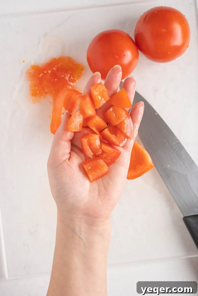 Vibrant Moroccan Tomato Salad 5 A hand holding a handful of diced tomatoes, showcasing their juicy texture, over a cutting board.