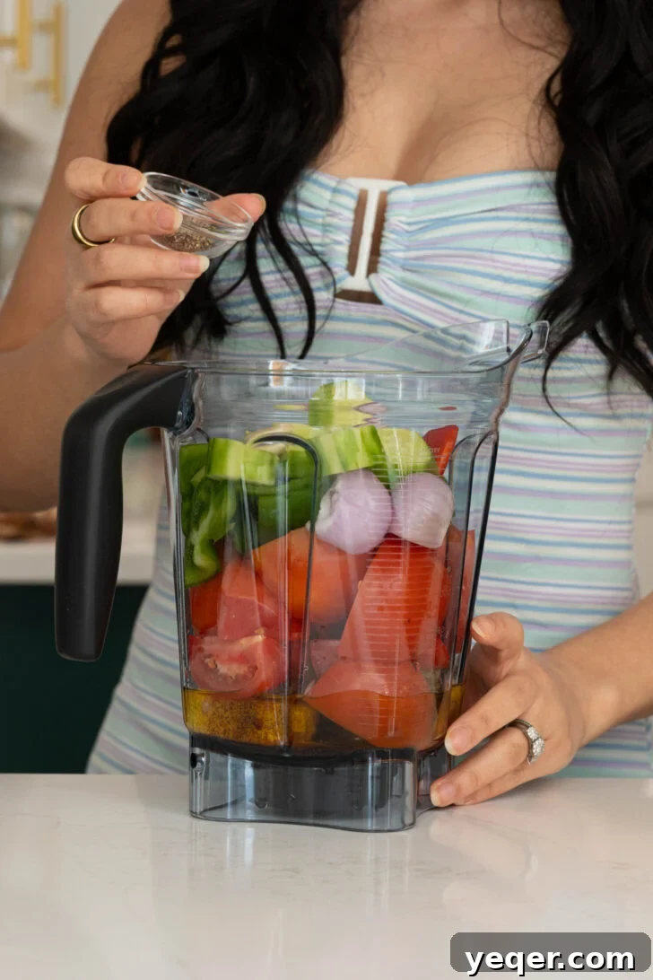 Classic Spanish Chilled Tomato Gazpacho 4 A person adding vibrant red peppers into a blender filled with other fresh gazpacho ingredients.